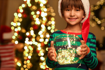 Little boy in Santa hat with garland at home on Christmas eve
