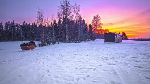 Beautiful day to night time lapse of snowy winter landscape and colorful sky during sunset - Fir trees,barell sauna and wooden cottage during vacation in Northern Europe