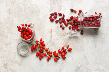 Jars of fresh rose hip berries on light background