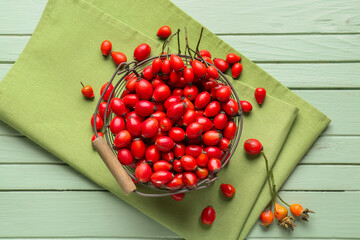 Basket with fresh rose hip berries on green wooden background