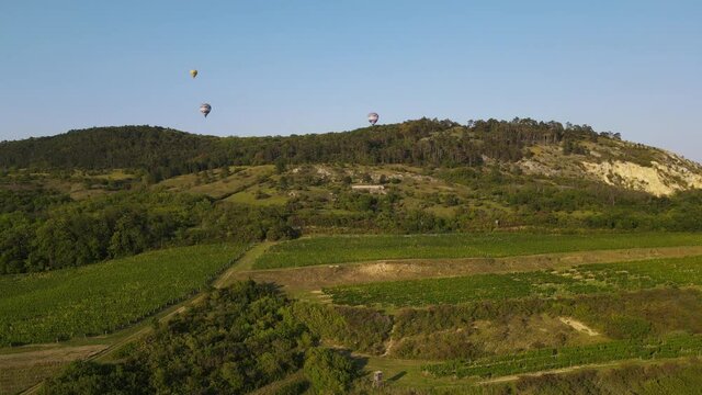 Aerial view of the landscape above which hot air balloons rise.