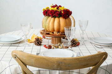 Beautiful bouquet of autumn flowers in pumpkin on served table near white wall