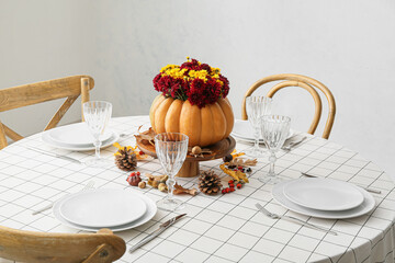 Beautiful bouquet of autumn flowers in pumpkin on served table near white wall