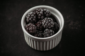 Frozen blackberry in ceramic bowl on rustic wooden background. Selective focus. Shallow depth of field.