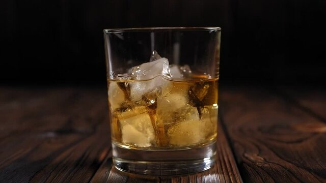 Glass of whiskey with ice on wooden table. Copy space. A glass of whiskey with ice on a wooden background in the dark with artificial lighting.