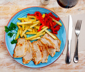 Delicious pork tenderloin steaks served with fried potatoes and sliced baked red pepper garnished with fresh parsley