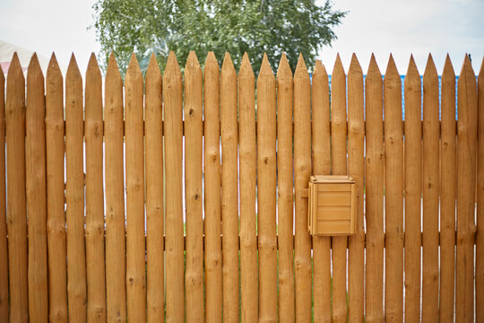 The fence is made of wooden planks in the form of a palisade, a mailbox hangs on it
