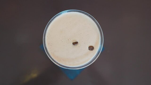 Hand placing three coffee beans on to foam of espresso martini, top down