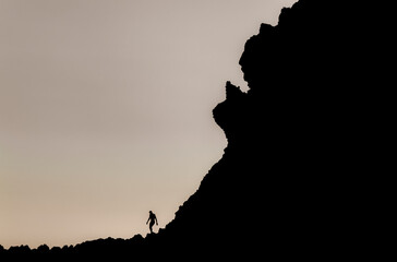 Silhouette of man climbing rock on beach during sunset