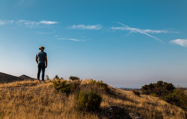 Naklejka na ściany i meble Rear view of adult man in cowboy hat looking at view in field against blue sky