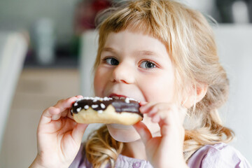 Happy little preschool girl eating sweet donut indoor. Blond child in the city. Cute kid and...