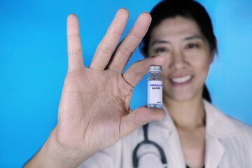 An attractive female doctor in white coat and stethoscope around her neck is holding a glass bottle...