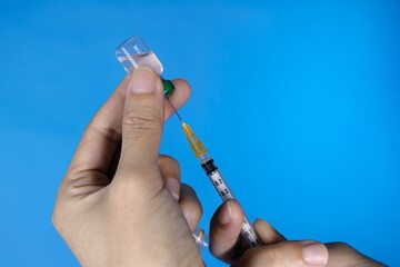 A closeup of doctor's hands holding syringe and a bottle of vaccine. Clear glass vaccine bottle.  Blue background. Healthcare And Medical concept.