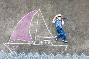 Little preschool boy as pirate on ship or sailingboat picture painting with colorful chalks on...