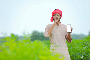 Young indian farmer showing smartphone screen at agriculture field.