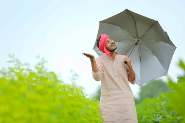 Young indian farmer using umbrella and walking at agriculture field.
