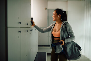 Happy Asian athlete takes her stuff from locker after finishing sports training at gym.