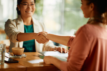 Close-up of businesswomen handshaking while greeting in cafe.