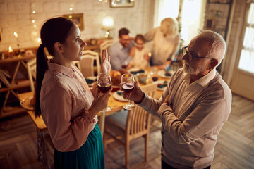 Senior father and his adult daughter talk and drink wine while celebrating Thanksgiving at at home.