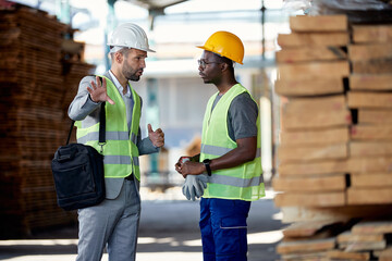 Warehouse manager talks to black worker at lumber distribution department.