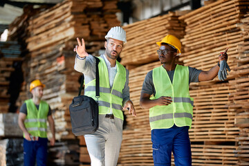 African American worker and businessman talk while walking through lumber warehouse.