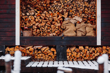 Barn with firewoods in snow. Saw and axe near firewoods.