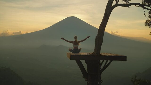 Woman lifting arms on platform doing yoga in front of majestic Mount Agung, sunset