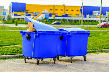 Two blue overfilled waste bins on wheels for collecting recyclable materials. Pollution and waste...
