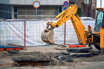Tractor bucket removes broken asphalt; repair underground communication. Excavator breaking asphalt...