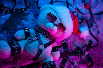 A toy bear in a Santa Claus hat is a Christmas gift for BDSM games in neon light