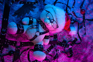 A toy bear in a Santa Claus hat is a Christmas gift for BDSM games in neon light