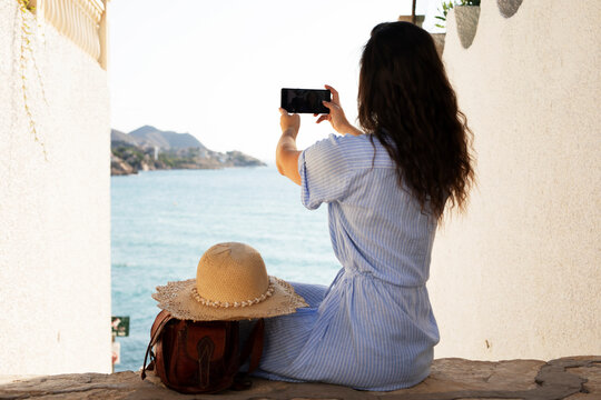 Young woman taking photo with phone near the sea. Happy woman enjoy in sunny day..