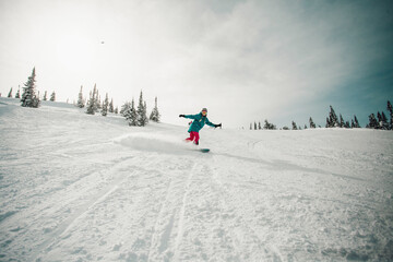 Young woman wearing blue and pink clothes snowboarding at almost empty tracks of Sheregesh ski...