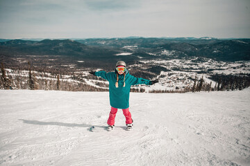 Young woman wearing blue and pink clothes snowboarding at almost empty tracks of Sheregesh ski...