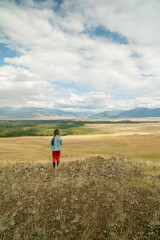 Naklejka na ściany i meble The girl in a picturesque place looks at the mountains and the steppe