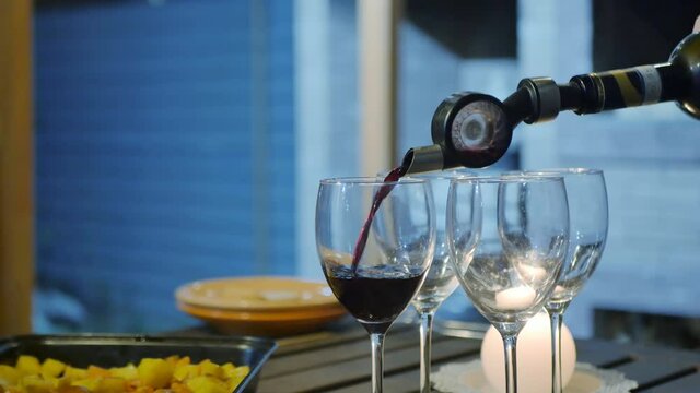 Red sweet wine is poured from the neck of a bottle with an aerator into glasses