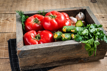 Fresh vegetables in a wooden box, red tomatoes, green cucumbers with herbs. Wooden background. Top view