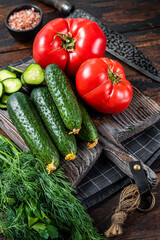 Cooking green vegetables salad with tomatoes, cucumbers, parsley, herbs. Dark wooden background. Top view