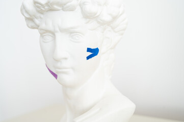 Gypsum statue of David head with kinesio tape. Face-taping, lifting treatment on face concept
