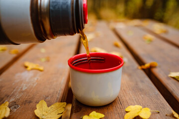 Cup of tea with autumn leaves reflection on wooden table. Season of autumn walk