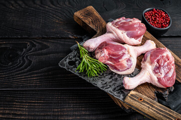 Raw Duck thighs on butcher board with meat cleaver. Black wooden background. Top view. Copy space