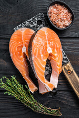 Fresh Raw Salmon steaks on butcher cleaver. Black wooden background. Top view