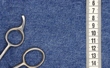 white measure tape and old scissors on blue jean fabric background