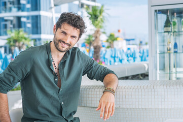 Young wide smiling man model portrait in outdoor beach bar