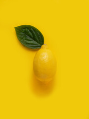 Lemon with a green leaf on a yellow background.