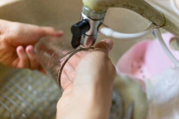 woman washes her glass under running water in the sink