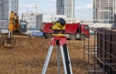Photo of a level at the construction site of multi-storey buildings with a yellow excavator and an red truck on the street in the city