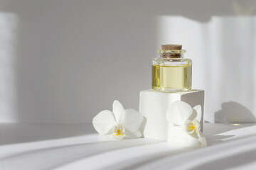 Mock-up of square bubble with essential oil on white 3d podium, surrounded by orchid flowers. Objects in rays of sunlight cast hard shadow on surface. Concept of spa treatments, body care