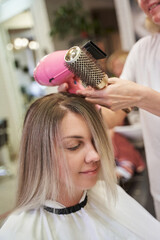 in the hands of a hairdresser, a hairdryer and a round brush next to the girl's blonde hair