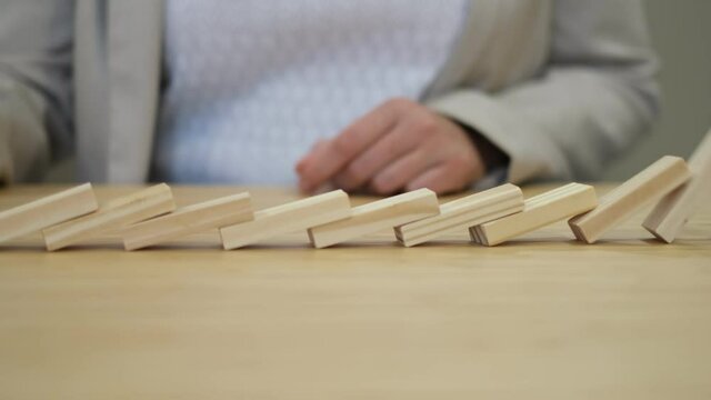 Hand of a business woman stopping falling dominos to prevent a total collapse and establish stability. Domino effect in business. System disruption